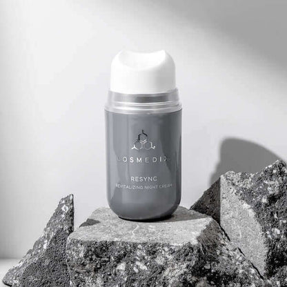 A bottle of Resync on rocks, it is a revitalizing Night Cream with antioxidant-rich extracts—like Snow Mushroom and Kakudu Plum—that quench skin with long-lasting moisture to help restore radiance and revitalize the look of skin, all while you sleep.